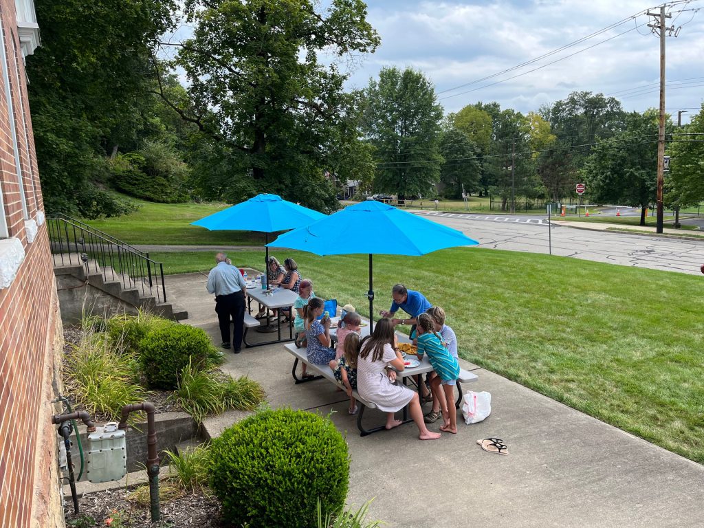 Church picnic at tables under blue umbrellas beside the Grace OPC building