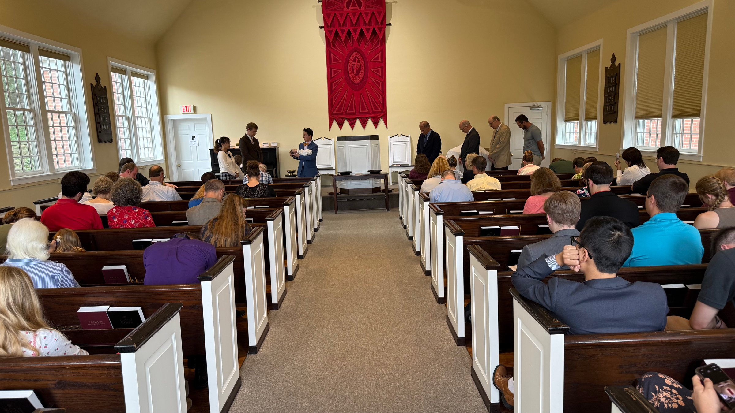 Grace OPC congregation in Sunday worship, seen down the center aisle toward the pulpit and red banner