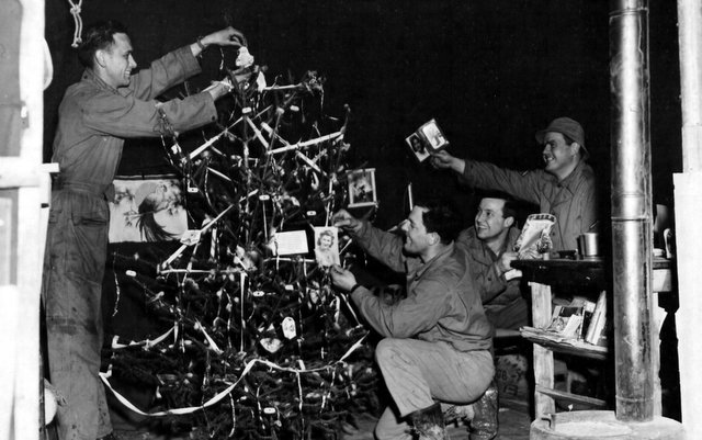 These GIs, attached to the 9th service command somewhere in England, take time out on Christmas Eve to decorate a tree at their base. They are, left to right: Pvt. George Rutter of Greenburg, Pa., Cpl. Conrad Myers of Fort Thomas, Ky., Cpl. Merrill Dunn of Laurel, Delaware, and Pfc. Edward Arnzen of Newport, Ky. 24 December 1943.