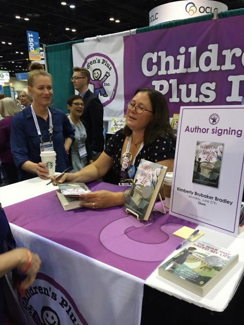 Kimberly Brubaker Bradley jotting a message on a copy of The War That Saved my Life at the Children's Plus booth