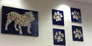 Wall canvases decorated with paint and magazine clippings. Students spray painted blank art canvases and traced on the bulldog and paw-print shapes. They filled the outlines by gluing on torn pieces from magazine pages.