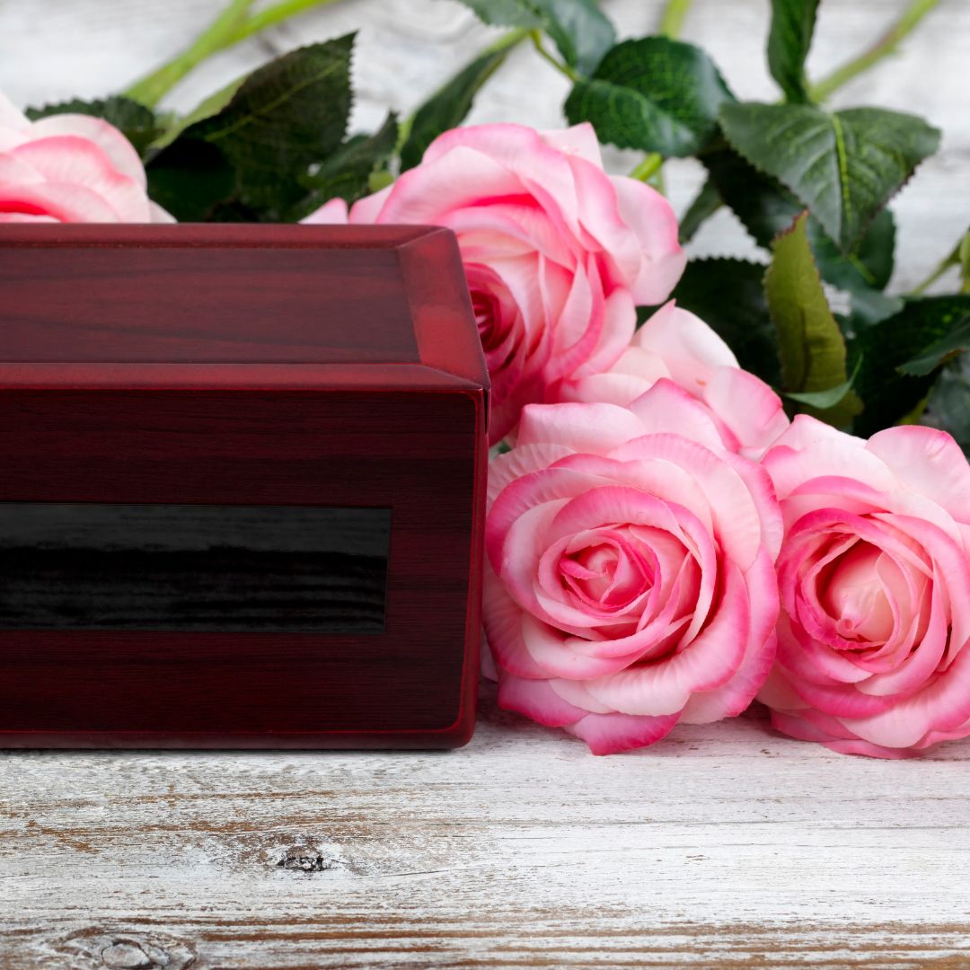 A wooden cremation box surrounded by pink roses