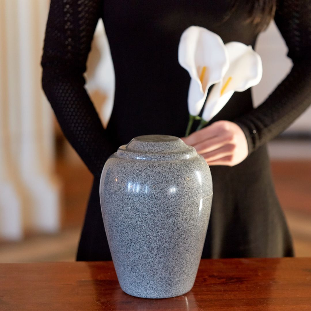 A person holding a flower standing next to an urn