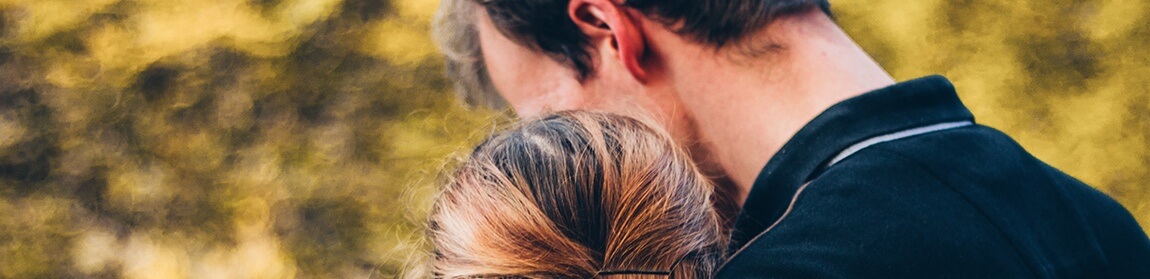 Grieving woman leaning on mans shoulder at funeral service.