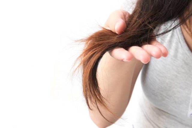 Mão feminina segurando mecha de cabelo danificado