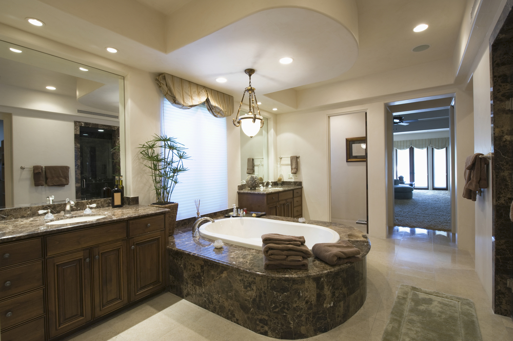Luxury bathroom with large tub in center in between two built-in dark wood vanities