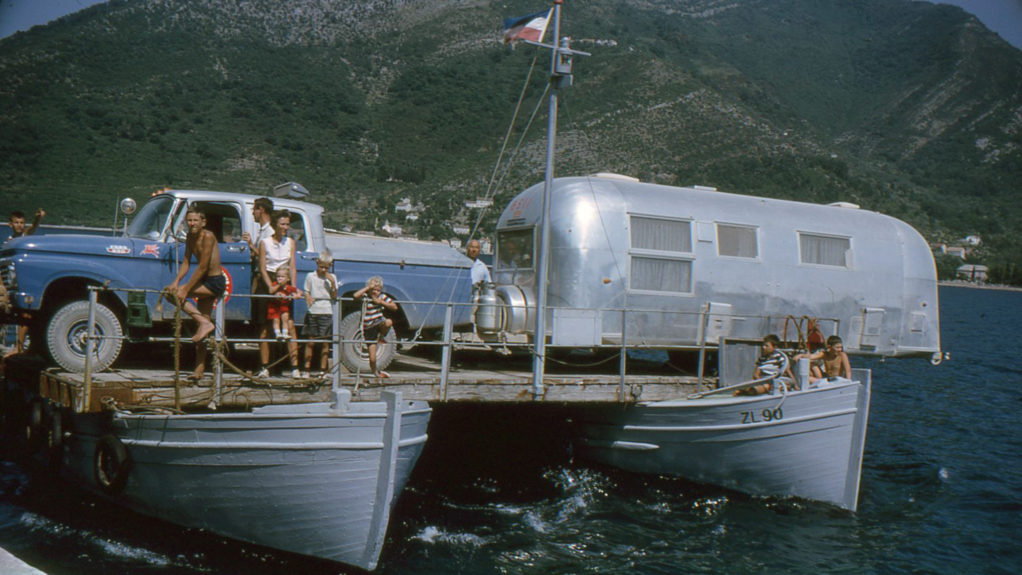 People on a boat that is carrying an Airstream travel trailer across the water during the Around the World Caravan.|The Smith family posing for a picture during the Airstream Around the World Caravan.|The first newsletter report about Airstream's Around the World caravan that was written by Mac Smith|People on a boat that is carrying an Airstream travel trailer across the water during the Around the World Caravan.|The Smith family in front of an Airstream Travel Trailer holding up an image from the Airstream Around the World Caravan|The Smith family looking through old photos of their Around the World Caravan with Airstream.