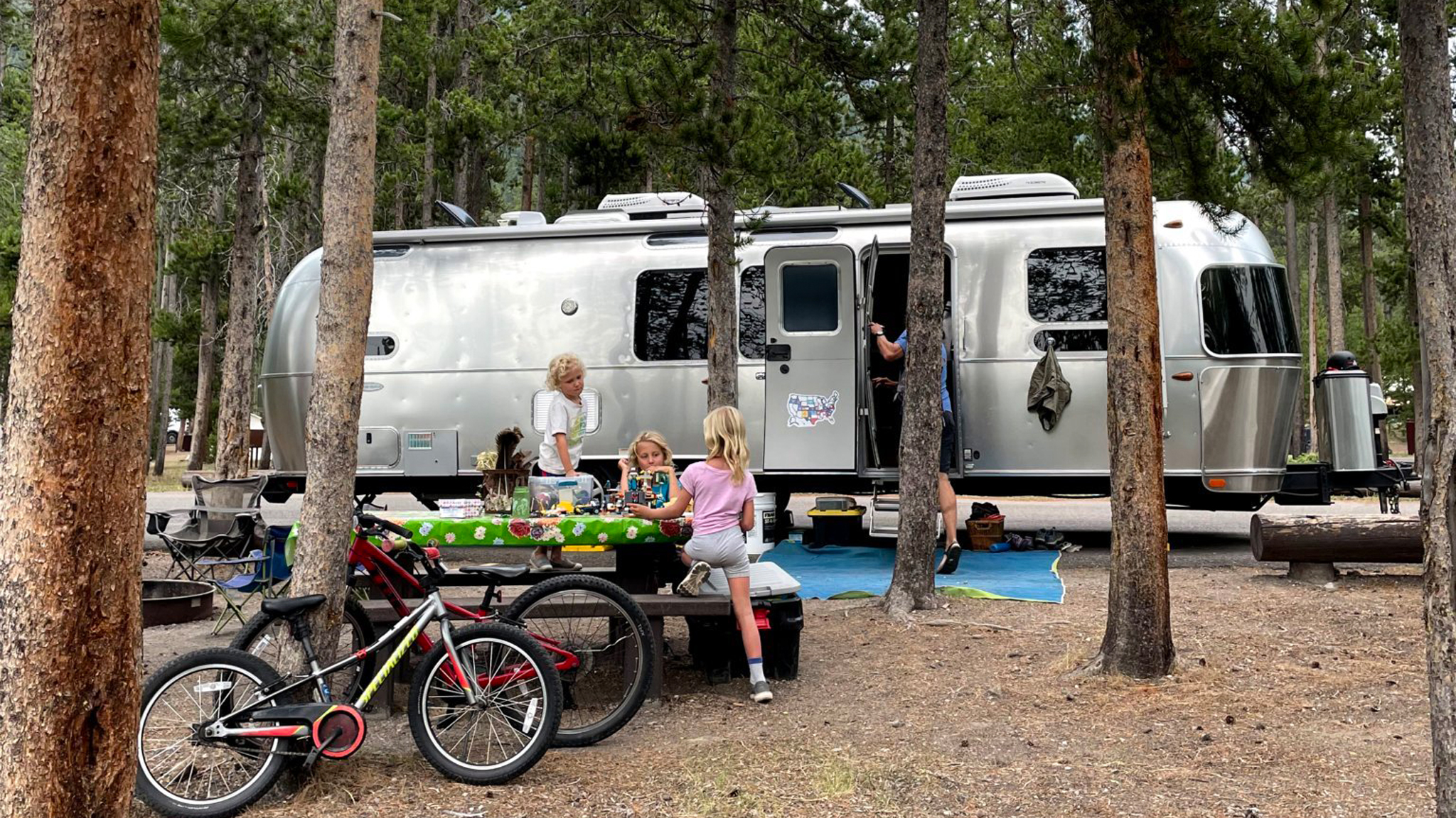Kids sitting on a picnic table and playing outside of their Airstream travel trailer while they camp.|Fajitas being cooked over a fire.|Two people sitting at a table cooking fish that they just caught.|Vegetables cooking on a grill over a fire.|Pasta noodles and sauce being cooked on a grill.|A plate of scones and a cup of coffee sitting on a table.|Four kids sitting at the table in an Airstream travel trailer eating dinner while they camp.|Three kids sitting at the table in their Airstream travel trailer playing go fish at night with a night light turned on.|A kid cooking fried rice on a grill while he camps in his Airstream Travel Trailer|Two kids on a scooter playing in the dirt while they boondock camp in their Airstream travel trailer|A little kid cooking french toast on a grill next to the Airstream travel trailer while a family camps.|Four kids watching a geyser while they camp.|Kids sitting on a picnic table and playing outside of their Airstream travel trailer while they camp.