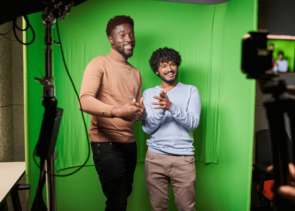 Two men standing in front of a portable green screen