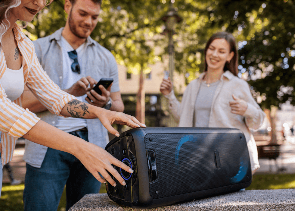 A small group of friends in the park, listening to music from a wireless speaker.