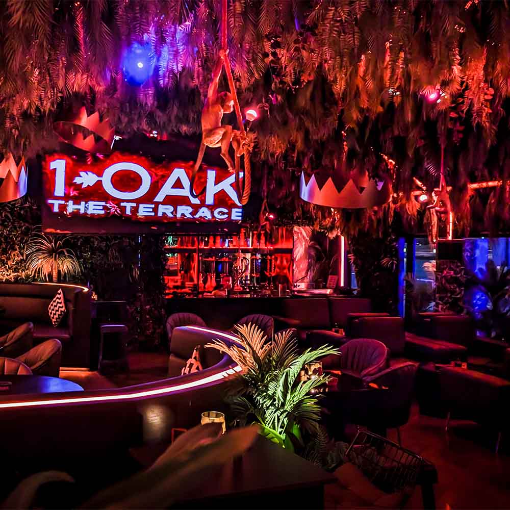 Vibrant interior of 1 OAK New York Nightclub, featuring lush foliage, colorful lighting, and a lively atmosphere.