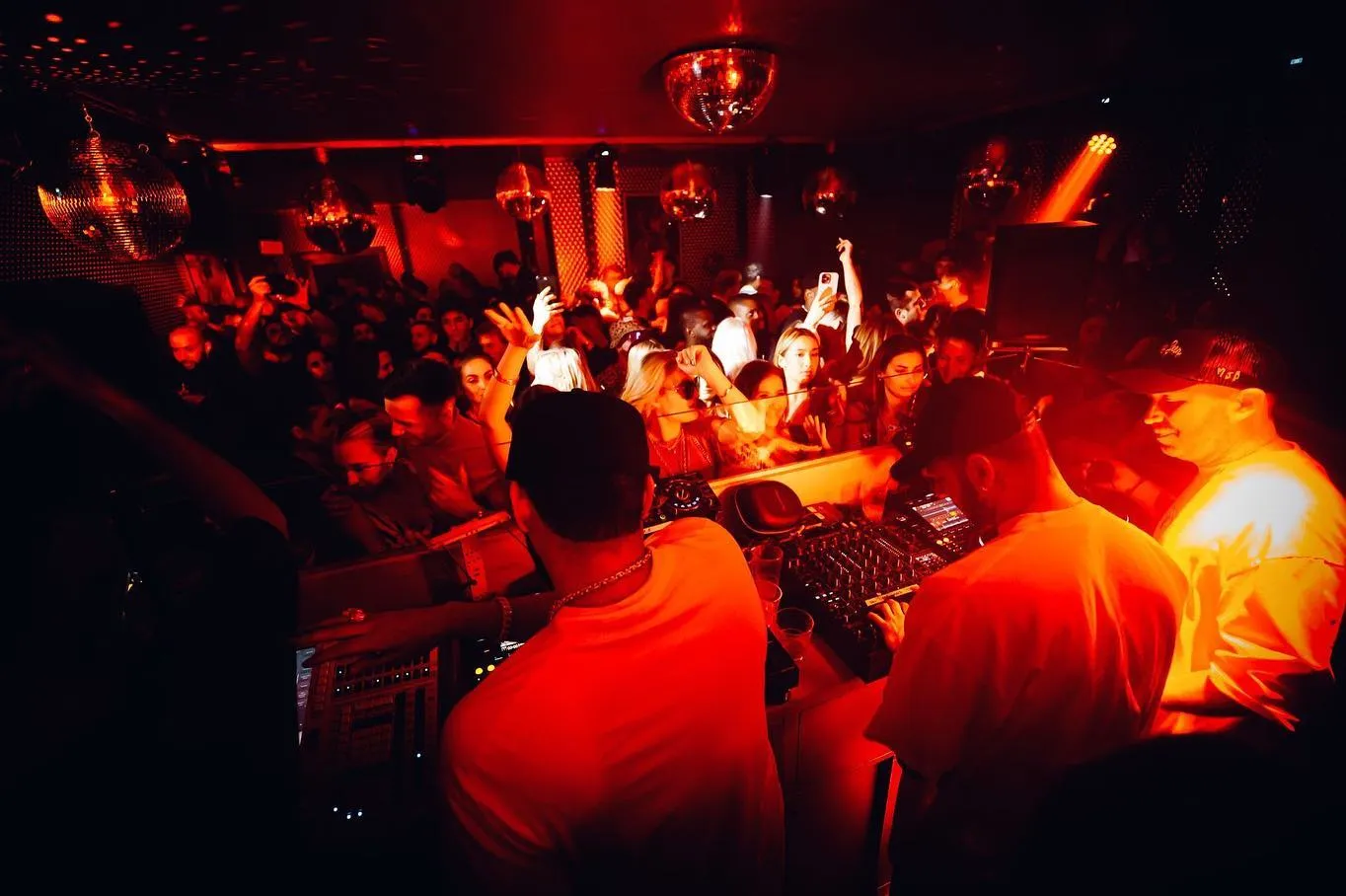 Vibrant nightclub scene with a crowd dancing under red lights, featuring a DJ at the decks in Raffles Chelsea London.