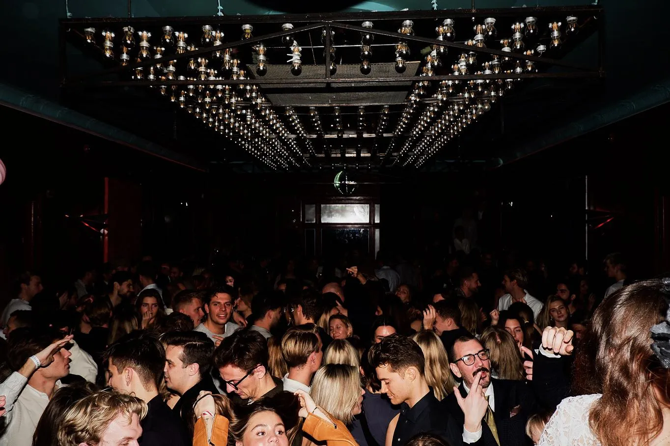 "Vibrant nightclub scene at Sø Pavillionen in Copenhagen, crowded with people dancing under a ceiling of glowing string lights."