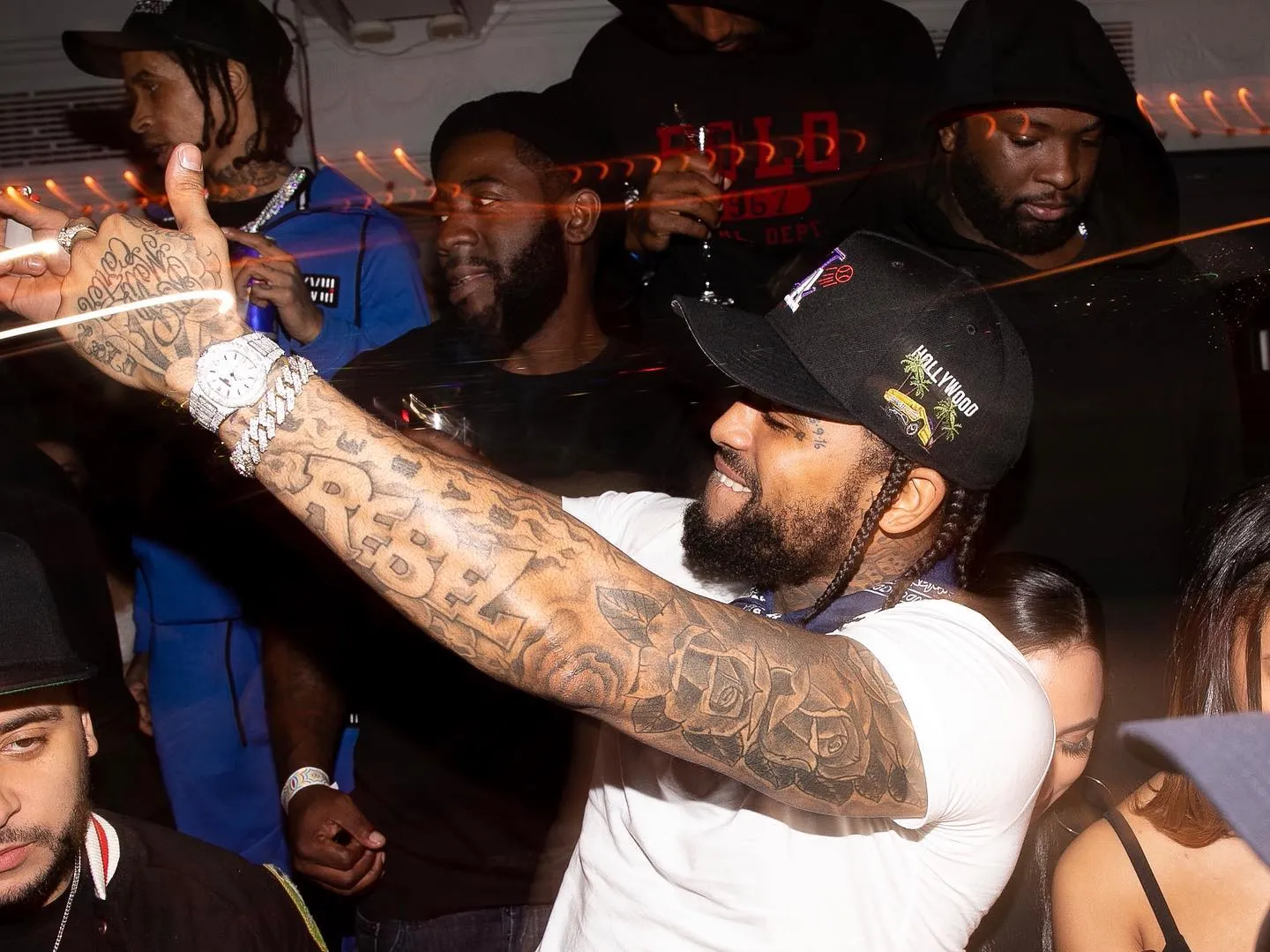 Vibrant nightclub scene with a tattooed man joyfully dancing, surrounded by partygoers enjoying drinks.