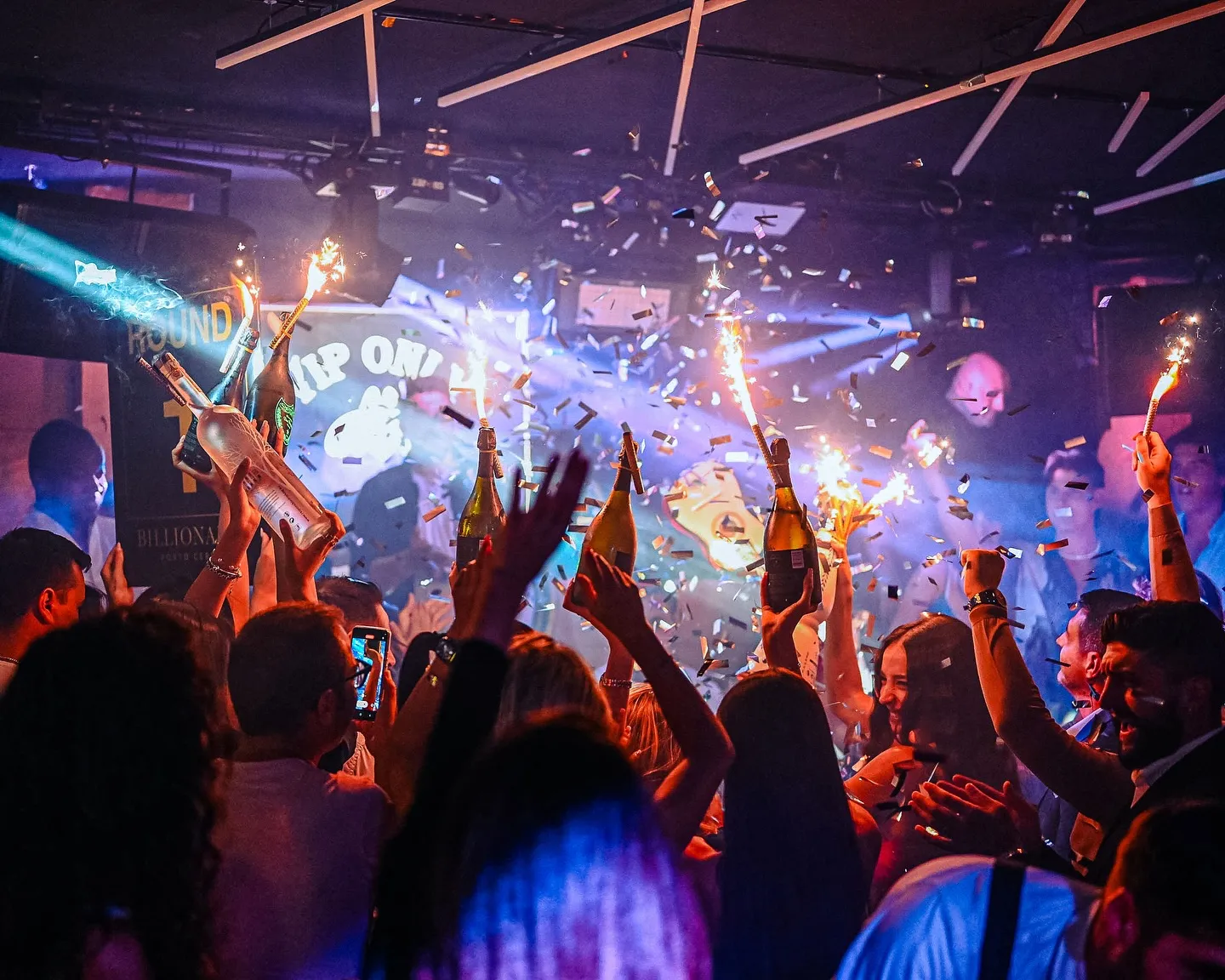 Vibrant nightclub scene at Billionaire Porto Cervo with lively crowd, sparkling confetti, and colorful lights.