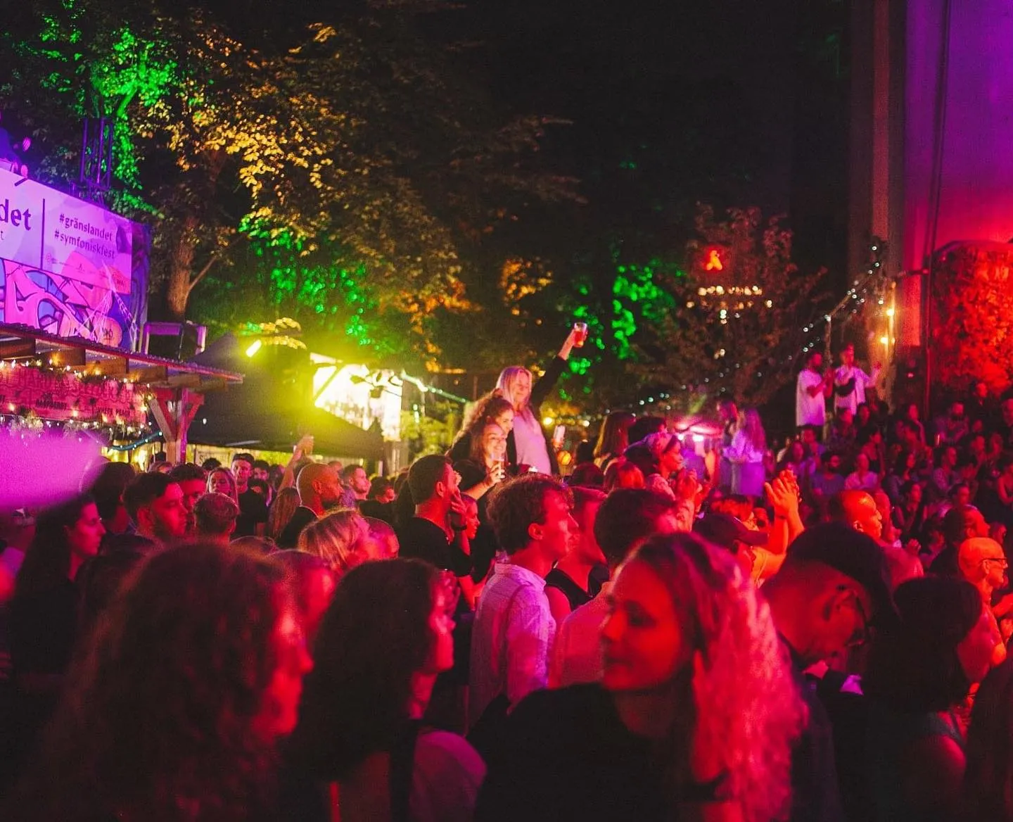 Vibrant crowd dancing at Trädgården nightclub in Stockholm, illuminated by colorful lights with a lively outdoor ambiance.
