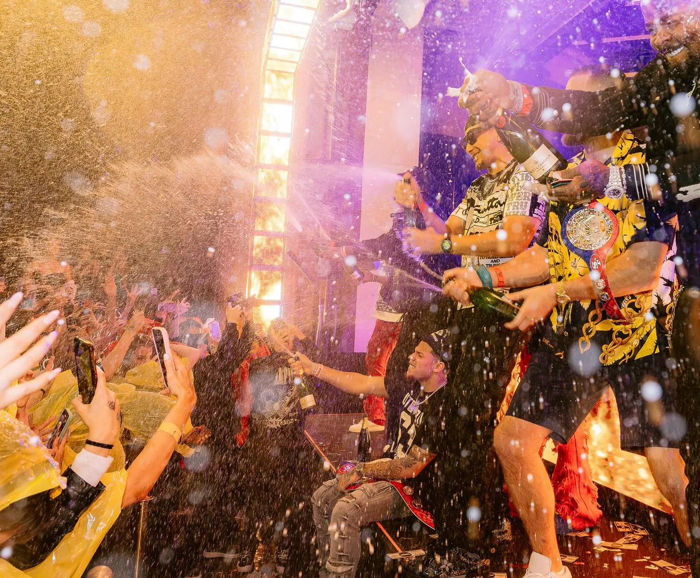 Vibrant nightclub scene at XS Las Vegas, featuring a crowd excitedly capturing the moment as performers spray champagne under dazzling lights.