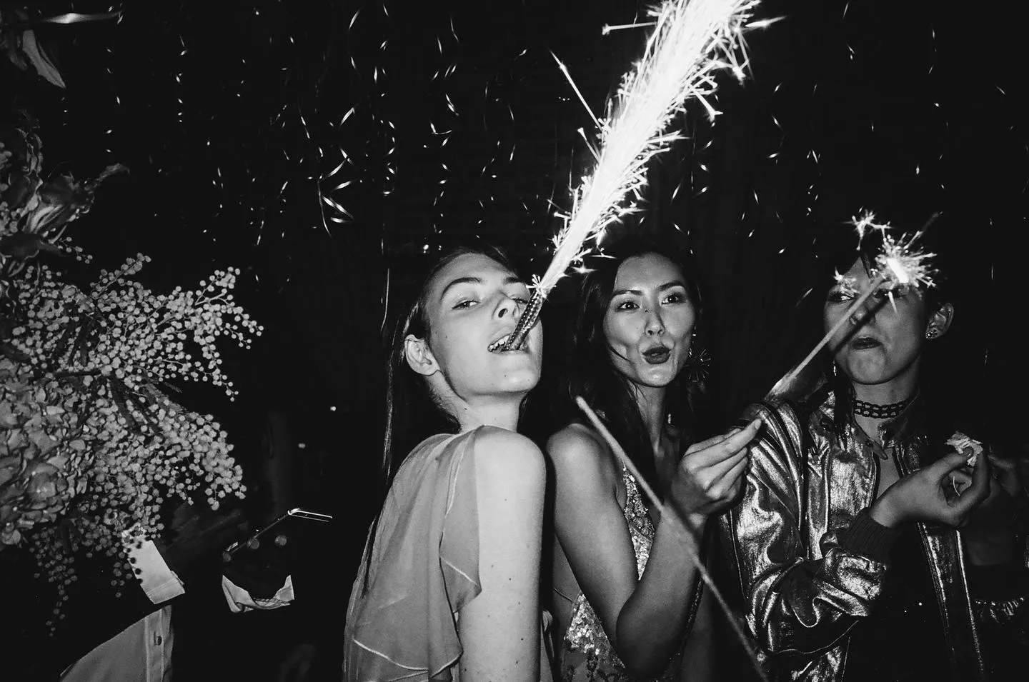Dynamic night scene at Up and Down New York nightclub with three people celebrating, featuring sparklers and energetic expressions, black and white photo.