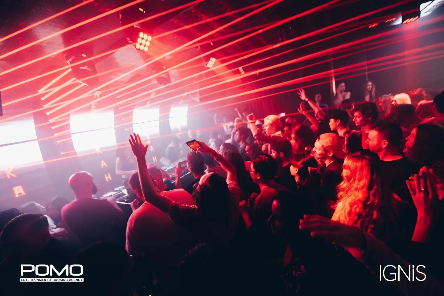 Vibrant nightclub scene at Ignis Hong Kong with a crowd dancing under red lights and dynamic beams, hands raised in excitement.