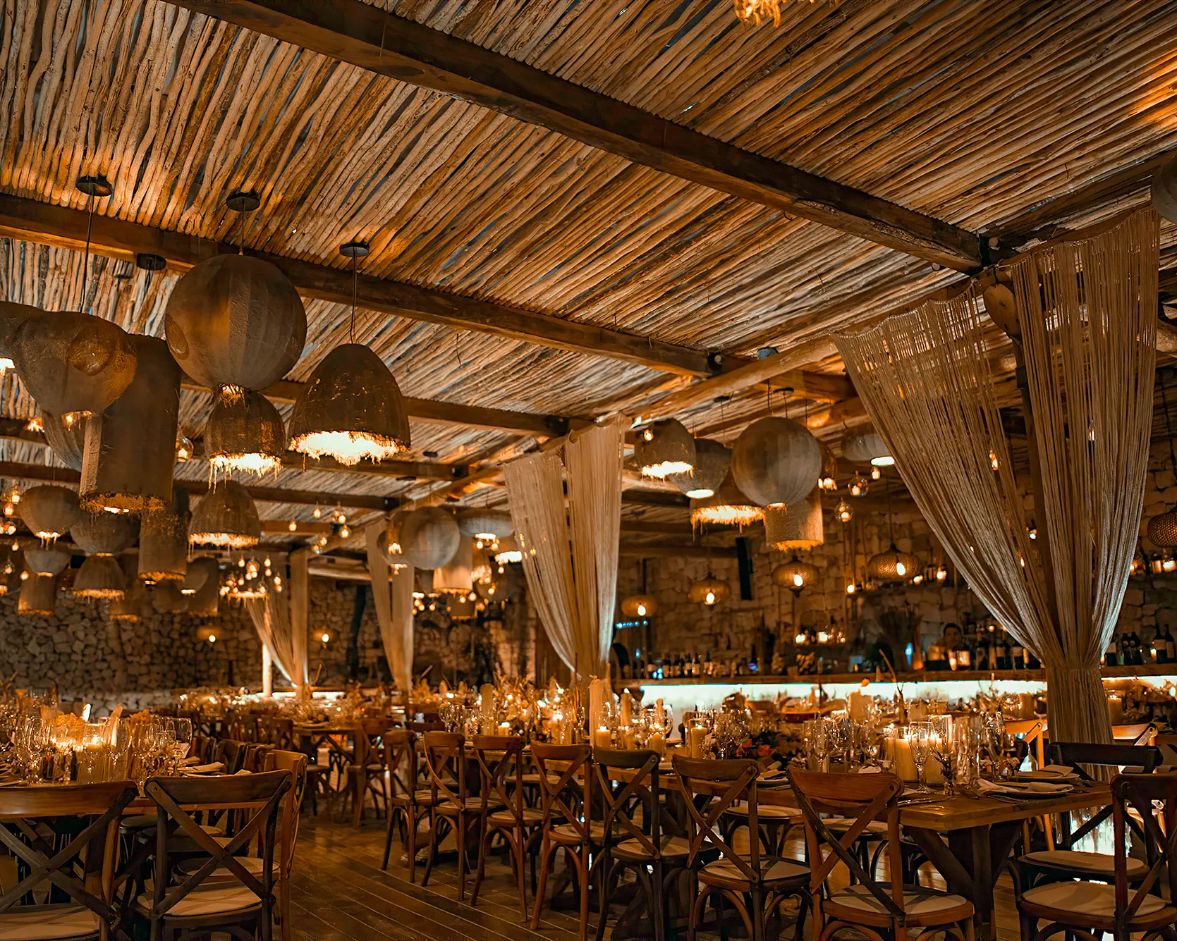 Inviting interior of Taboo Tulum, featuring rustic wooden tables, elegant light fixtures, and warm, ambient candlelight.