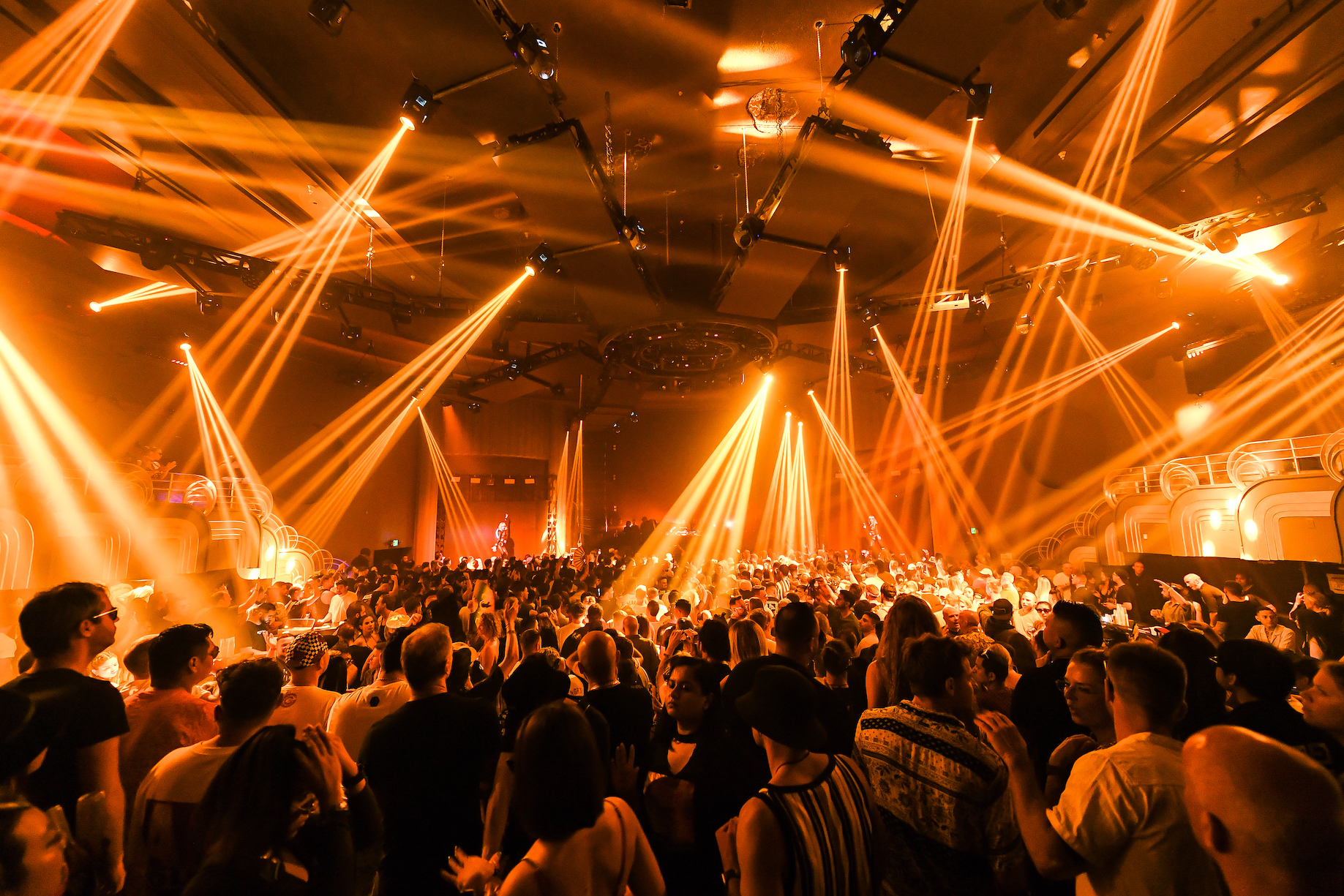 Vibrant nightclub scene at Do Not Sit Miami, filled with enthusiastic crowd bathed in dynamic orange lights and laser beams, capturing an electric nightlife atmosphere.