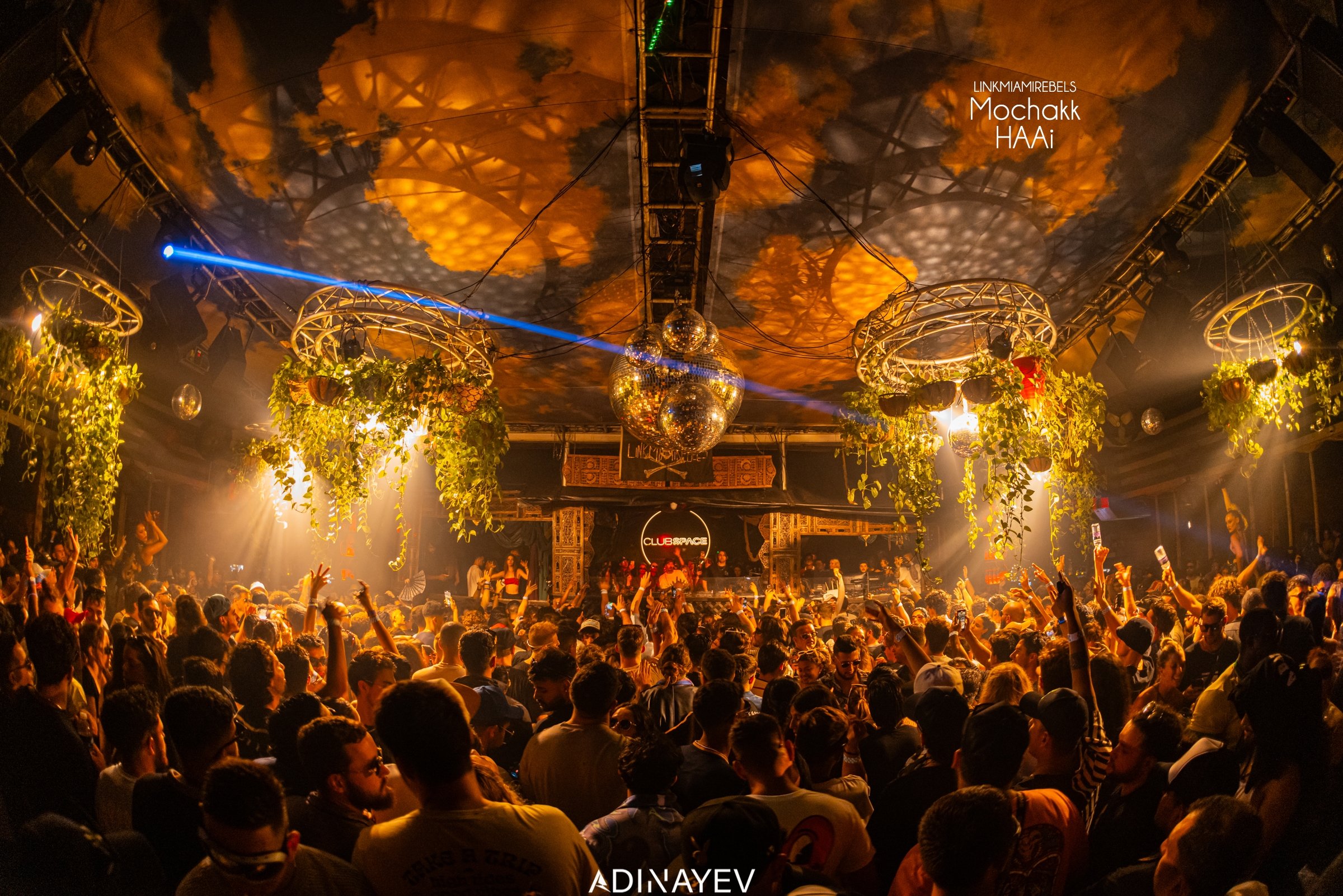 Vibrant rooftop scene at Club Space Miami, with a crowd dancing under a large disco ball, atmospheric lights, and lush hanging plants.
