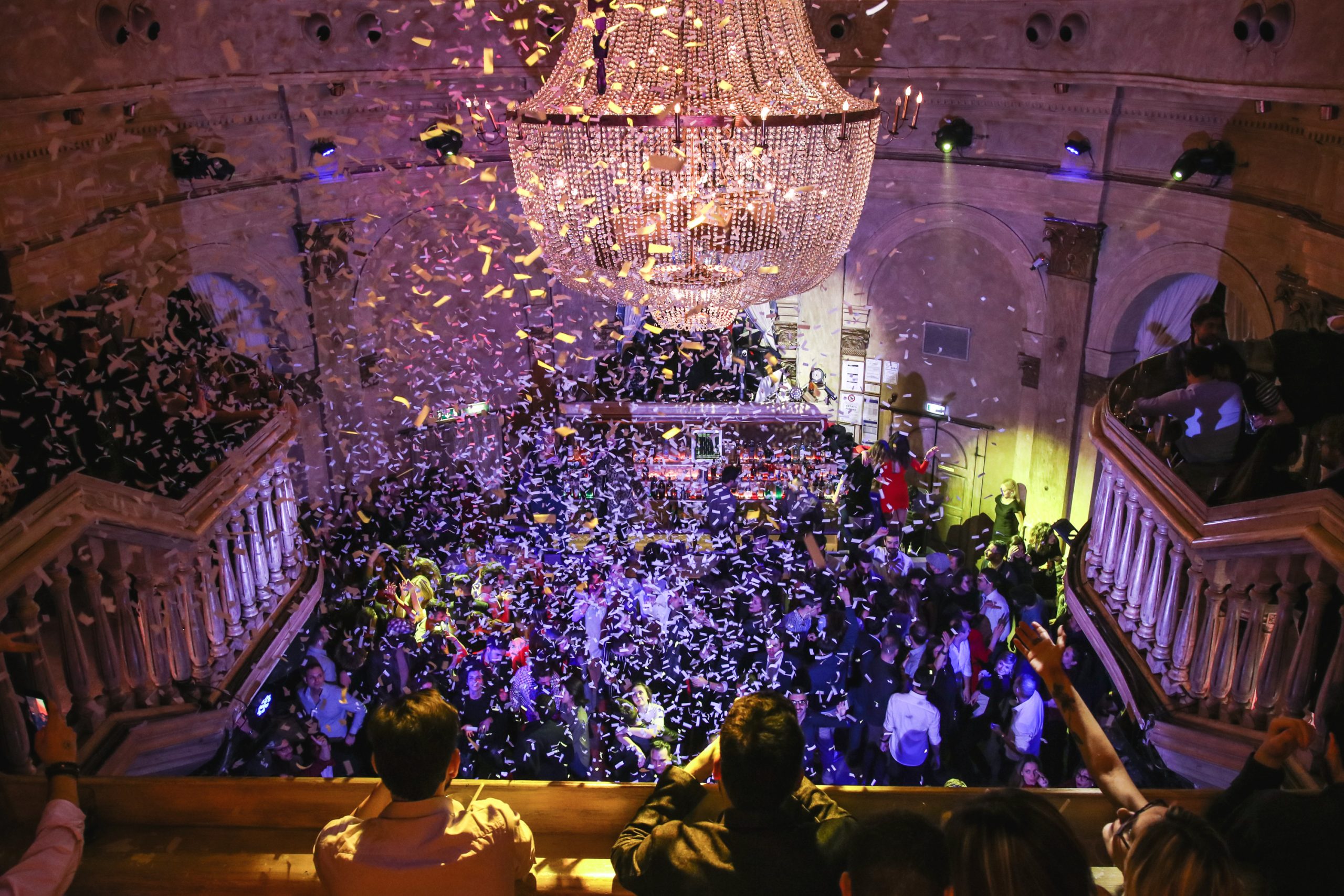 Vibrant nightclub scene at Gattopardo Milan with a large crowd under a grand chandelier, confetti flying in air, capturing an exhilarating party atmosphere.