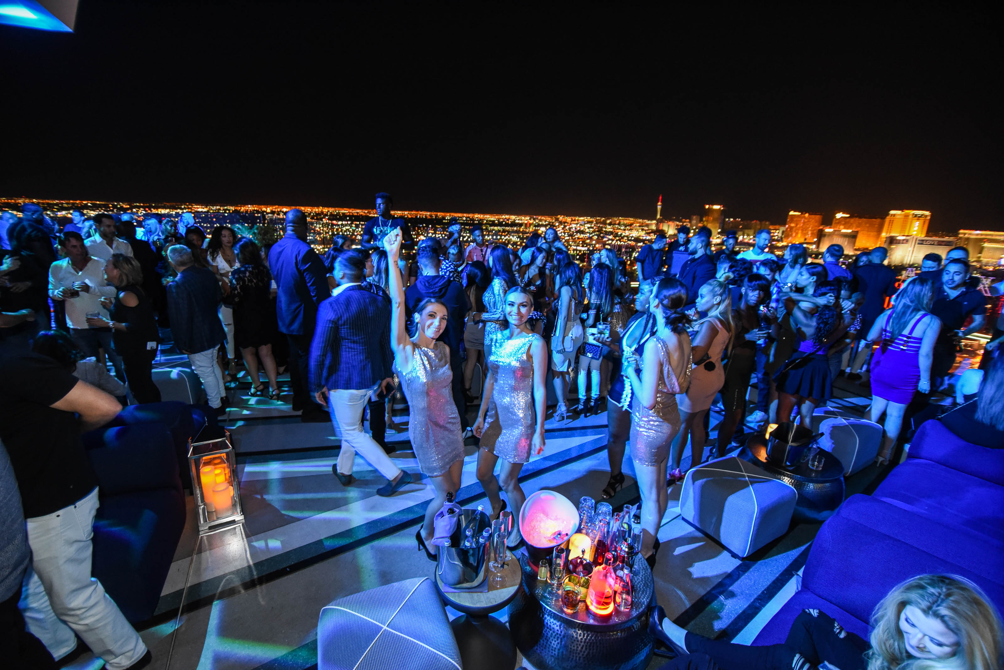 Vibrant rooftop party at Apex Social Club in Las Vegas, with lively crowd, dazzling city lights in the background, and a festive atmosphere.