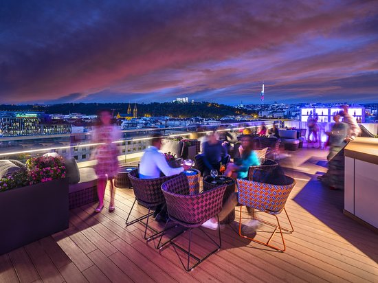 Stunning view from Cloud 9 Sky Bar in Prague at dusk, featuring vibrant skies and city lights, with guests enjoying drinks and conversation.