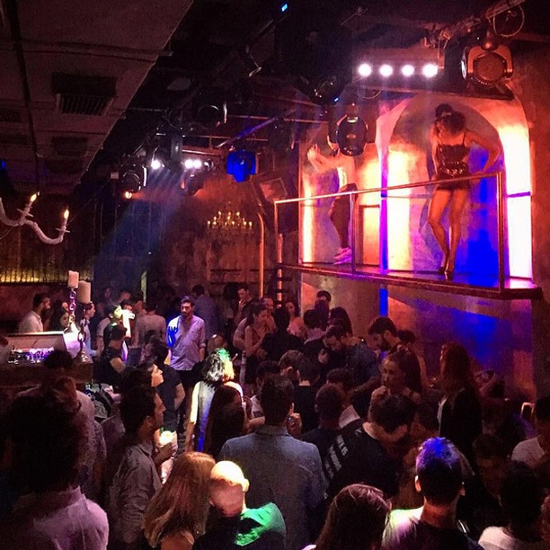 Vibrant scene inside Moni Mykonos nightclub, featuring a crowd of people enjoying the night with dynamic blue and purple lighting and large artistic murals.