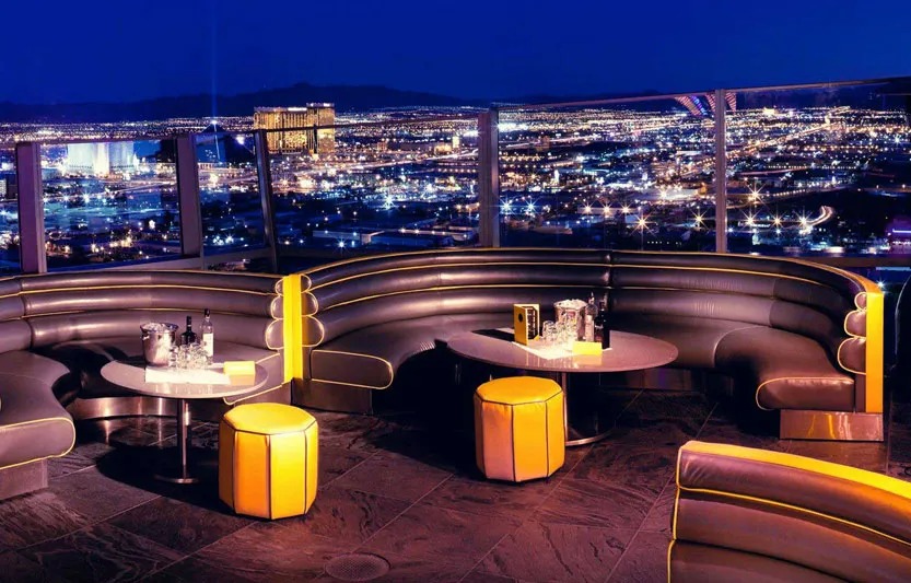 Alt caption: Plush curved seating and glowing tables at GhostBar, with a stunning panoramic view of the Las Vegas city lights at night.