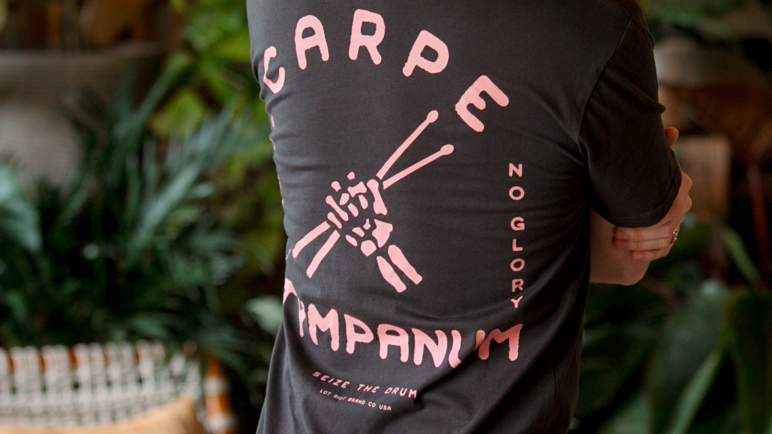 close up of a man wearing a black t-shirt with pink drum sticks printed on the back