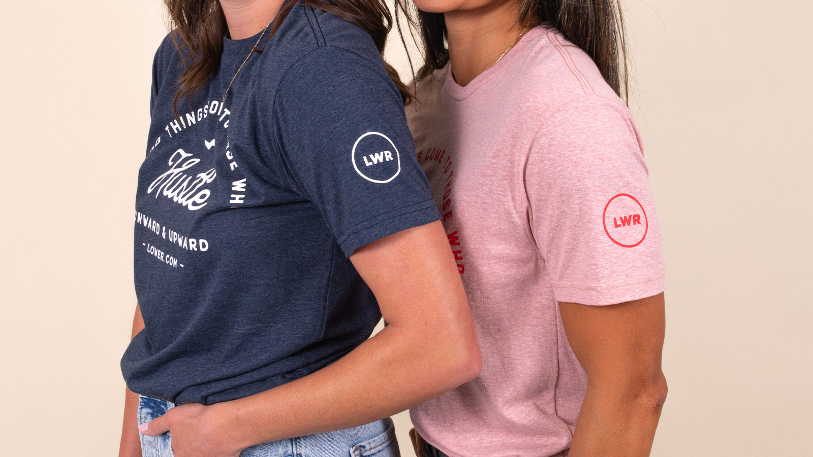 Two women with their left side facing the camera. One wearing a navy t-shirt and a pink t-shirt.