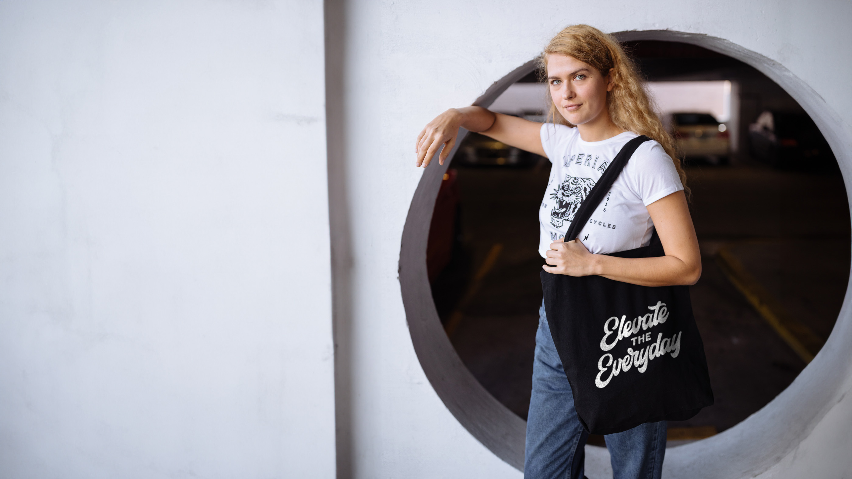 women wearing a white shirt and holding a black tote bag with the words "elevate the everyday" printed on it