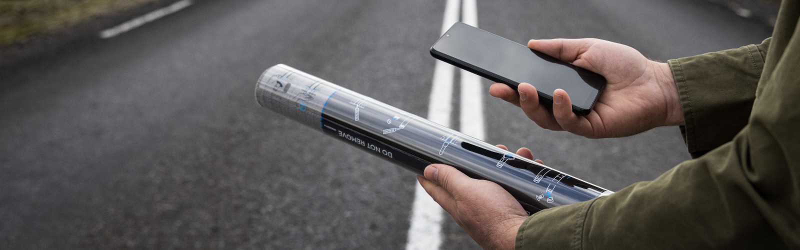 Man holding a GroundCast sensor in one hand and a mobile phone in the other.