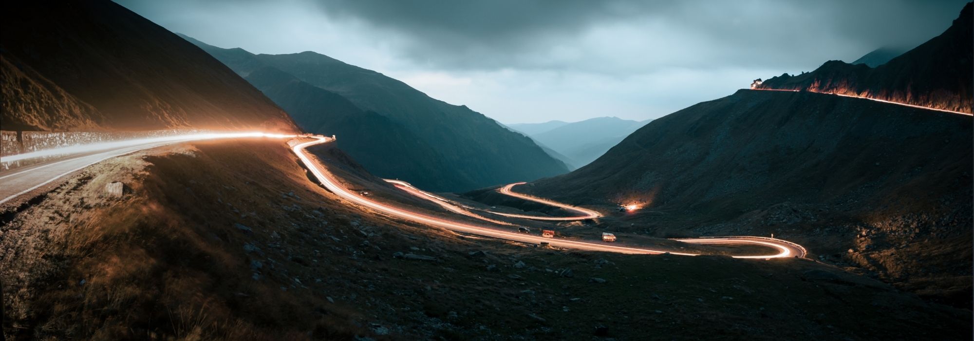 Long-exposure photo with a bright ribbon of vehicle headlights following a winding mountain road