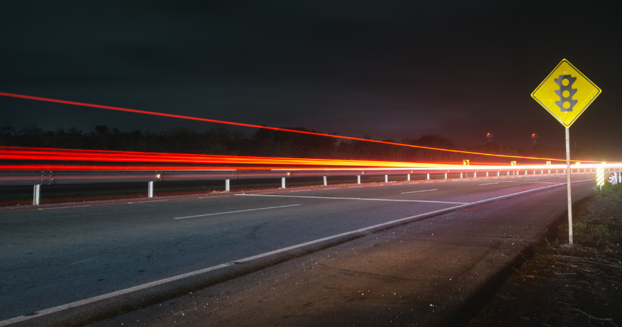 Long-exposure image of red tail light trails receding into the distance at night