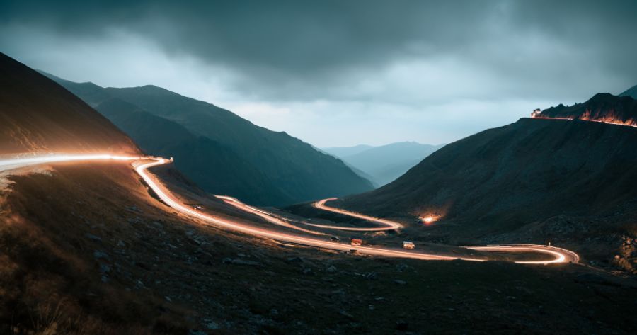 Long-exposure photo with a bright ribbon of vehicle headlights following a winding mountain road