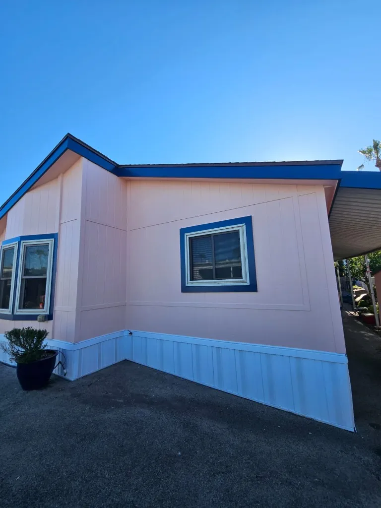 Mobile home corner view with pink paint and blue trim — exterior painting complete