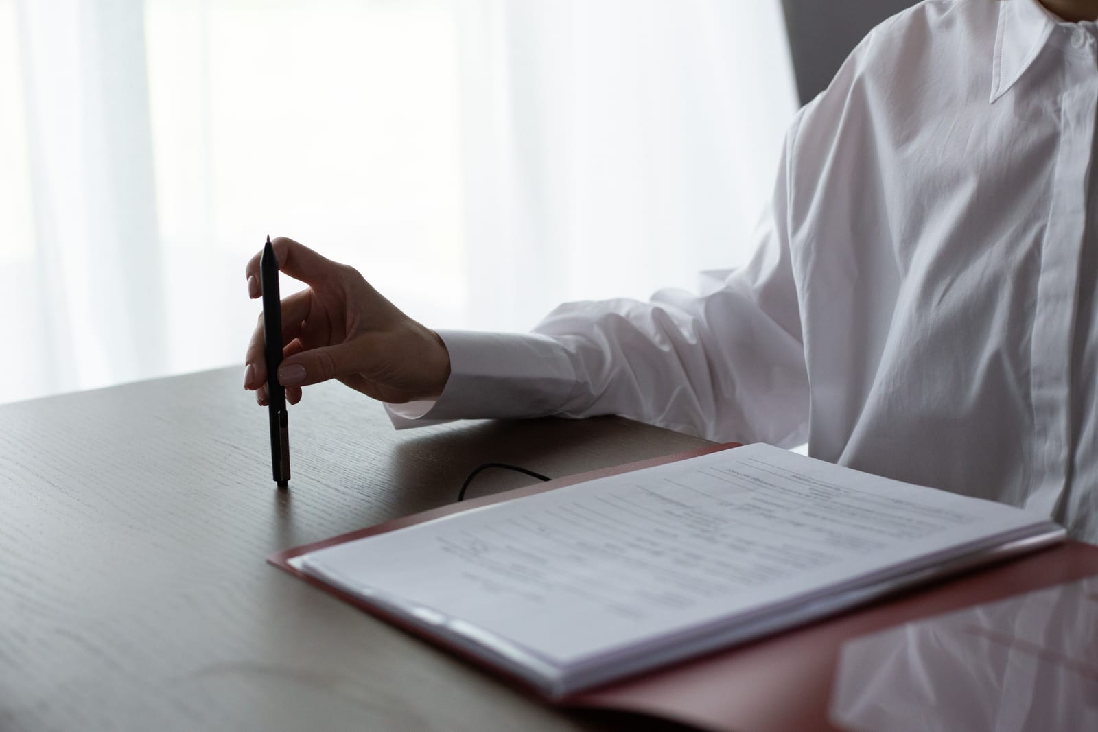 A hand holding a pen over a printed contract on a desk