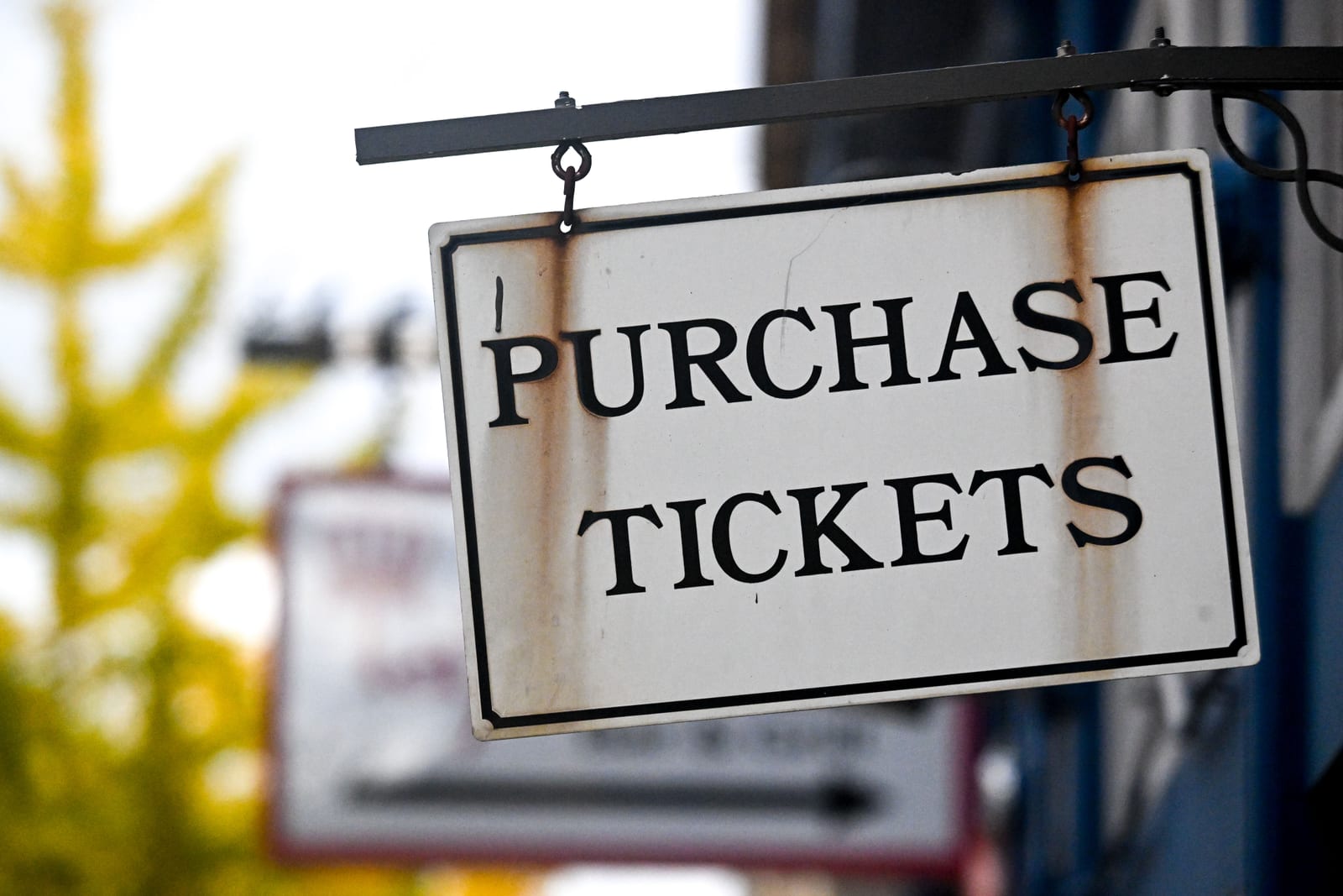 A weathered enamel sign reading Purchase Tickets hanging from an iron bracket A weathered enamel sign reading Purchase Tickets hanging from an iron bracket
