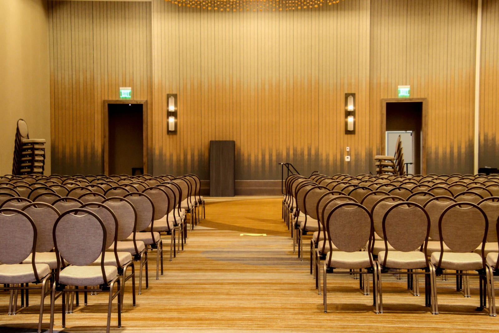 Empty conference ballroom set with rows of chairs, with more chairs stacked at the sides ready to be added Empty conference ballroom set with rows of chairs, with more chairs stacked at the sides ready to be added