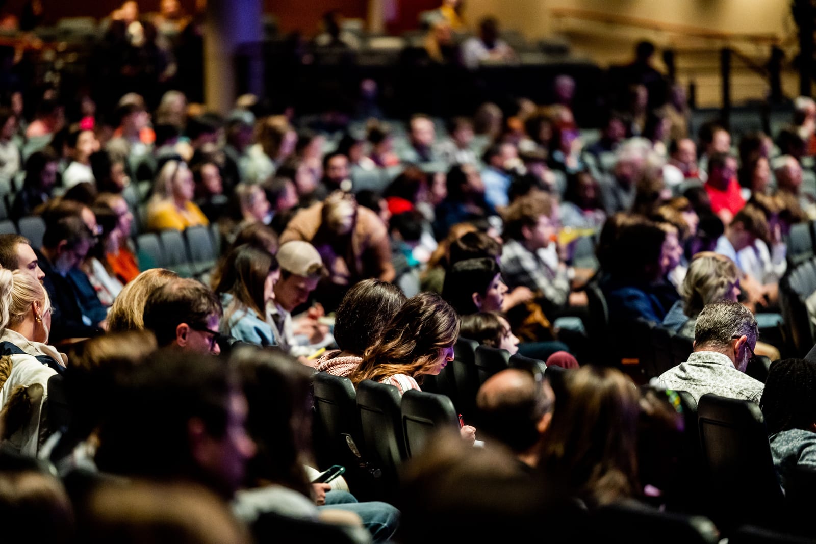 A packed auditorium audience seen from the side, rows filled to the back wall A packed auditorium audience seen from the side, rows filled to the back wall