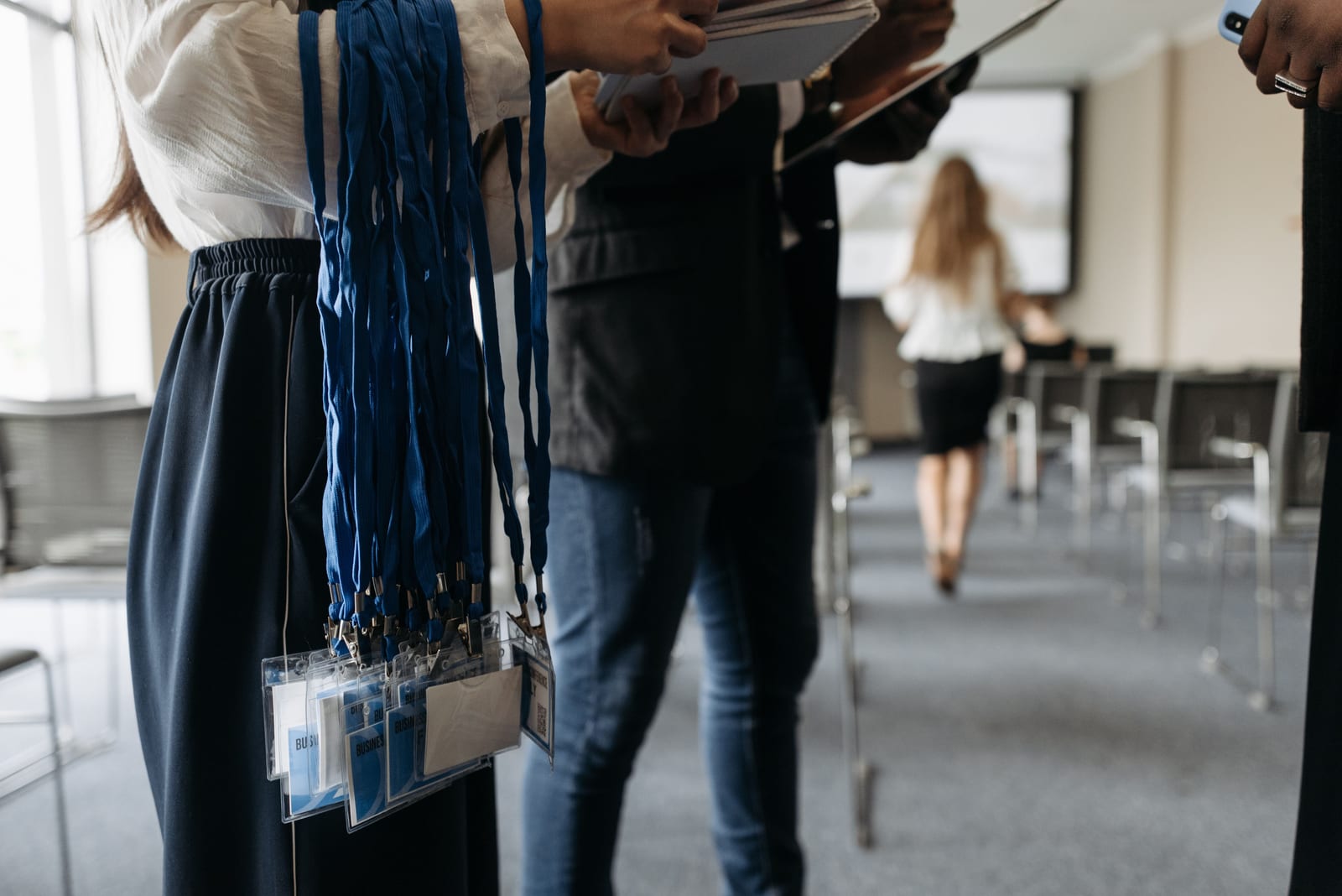 Two event staff holding a bundle of lanyards and badges in a conference room before doors open Two event staff holding a bundle of lanyards and badges in a conference room before doors open