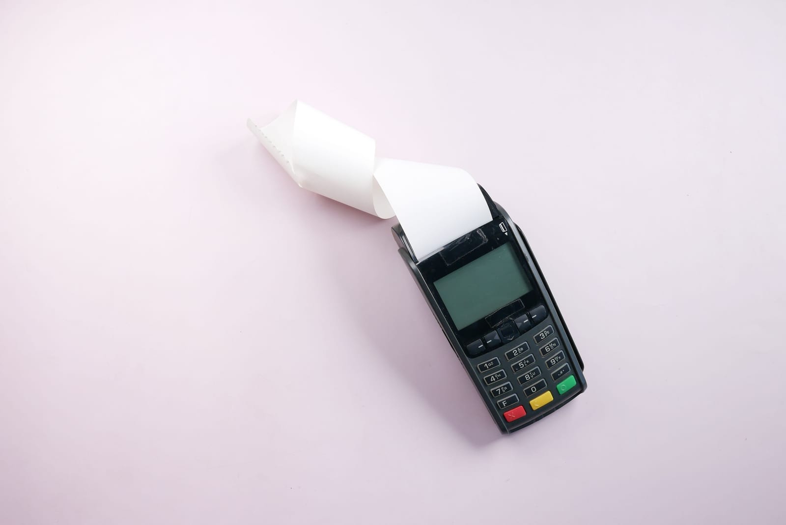 A card payment terminal on a pale pink surface with a blank receipt curling out of the printer A card payment terminal on a pale pink surface with a blank receipt curling out of the printer