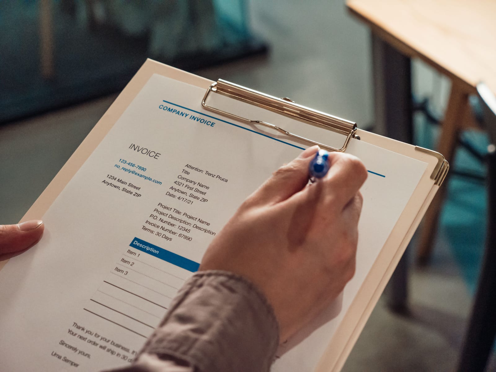 A person's hand writing on a blank company invoice attached to a clipboard A person's hand writing on a blank company invoice attached to a clipboard
