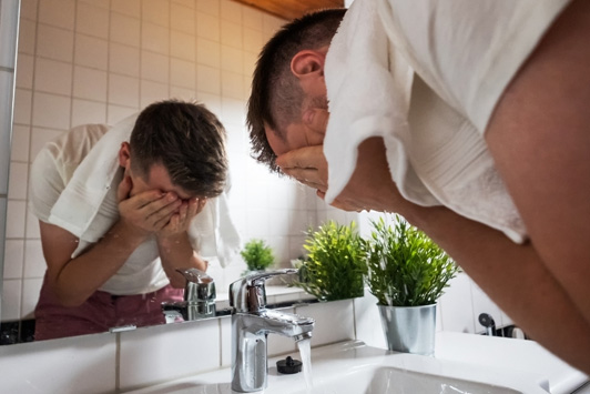 man washing face in sink