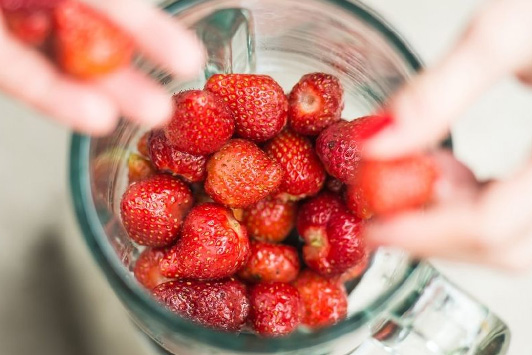 person putting strawberries into a blender