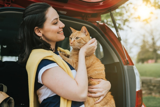 woman holding cat near car trunk