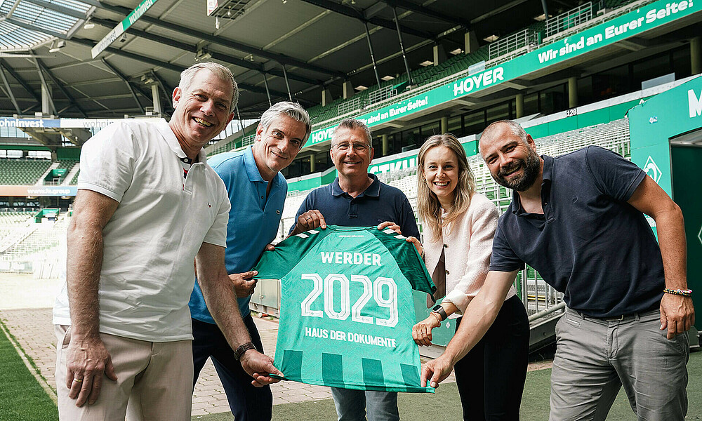 Mehrere Personen halten ein Trikot in den Händen.